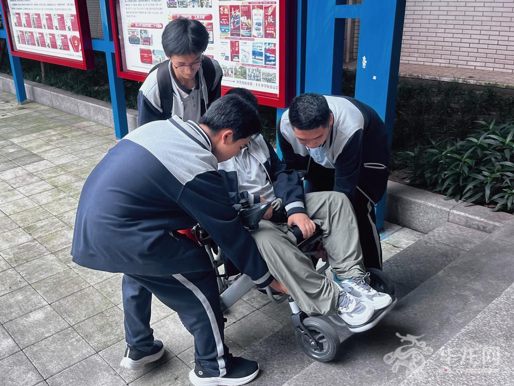 同学们正在帮助坐在轮椅上的石济瑞下楼梯台阶。 第1眼TV-华龙网 任璐瑶 摄